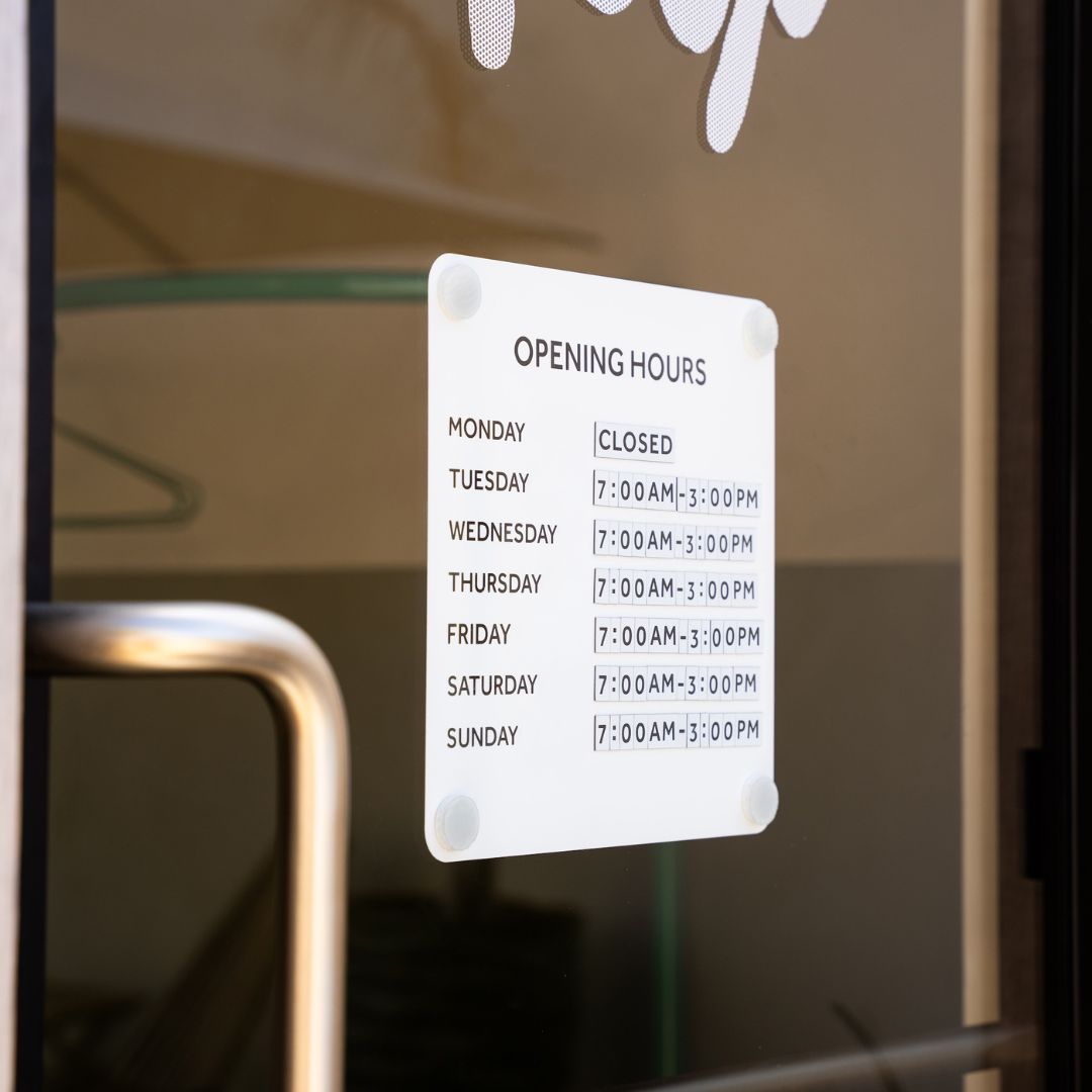 white opening hours sign mounted to window cling